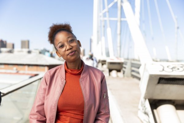 African woman wearing pink jacket on Nelson Mandela bridge grinning
