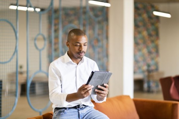 Black man looking at his tablet by the couch at work