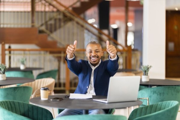 Black business man holding thumbs up at the office with a smile on his face