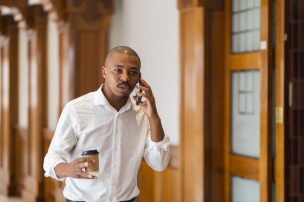 Black business man at work holding coffee and talking on the phone