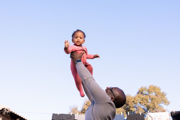 black daughter playing with father outdoors wearing pink with a blue sky in the background,