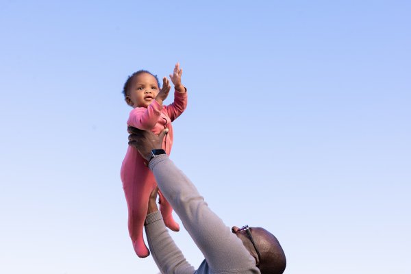 Black father holding daughter in the air with blue sky in the background in South Africa.