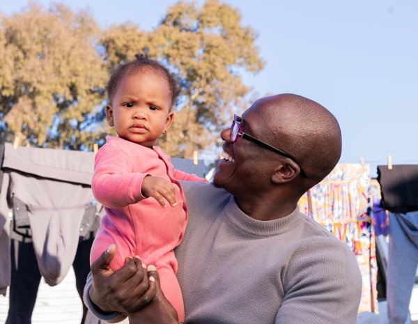 Black father smiling with daughter wearing pink and clothes hanging in the background