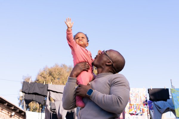 Black father with daughter playing outside with clothes in the background.