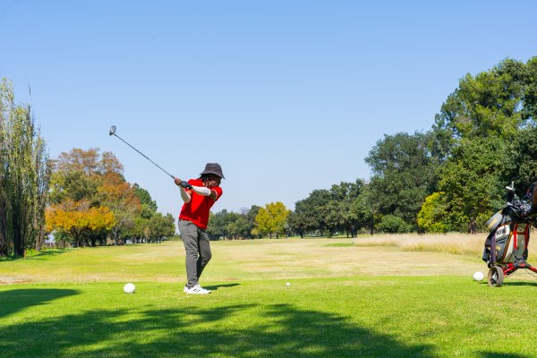 Black male golfer wearing a red golf shirt on the golf course hitting the ball