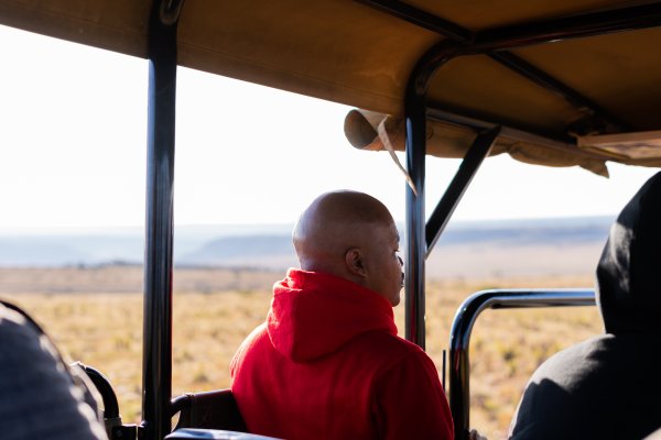 Black man in a safari car wearing a red jacket.