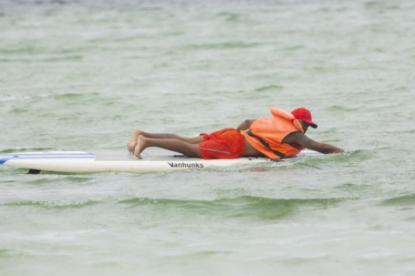 Black man on a surf board in a lagoon.