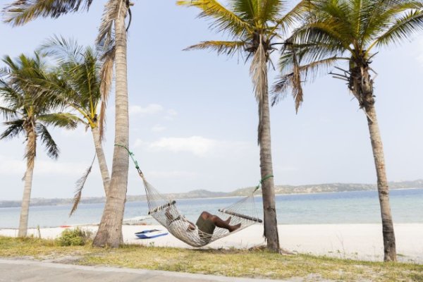 Black man resting on a hammock near a lagoon.