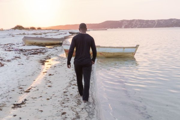 Black man walking near a lagoon with boats.