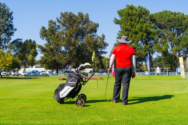 Black man wearing a red golf shirt with a Taylormade bag