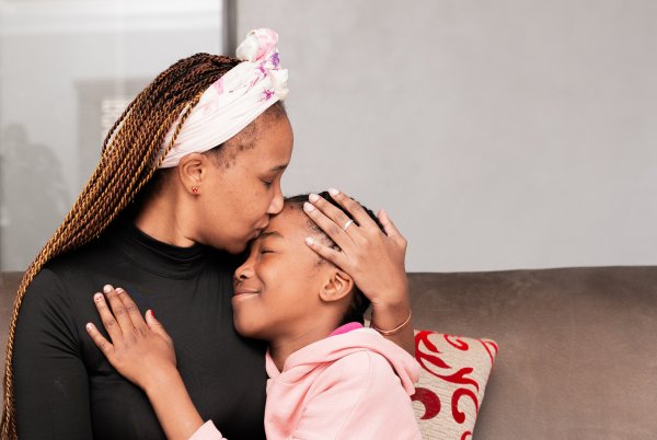 Black mother hugging daughter on the couch at home smiling.
