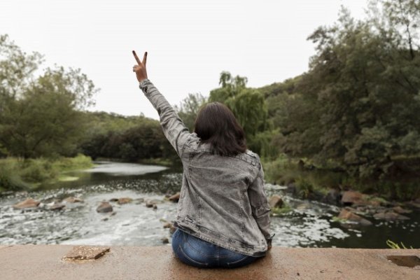 Black woman holding up peace sign by the river