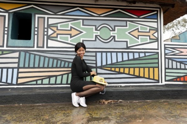 Black woman posing in front of Ndebele painting