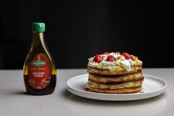 golden syrup bottle next to a plate of pancakes with strawberries and cream
