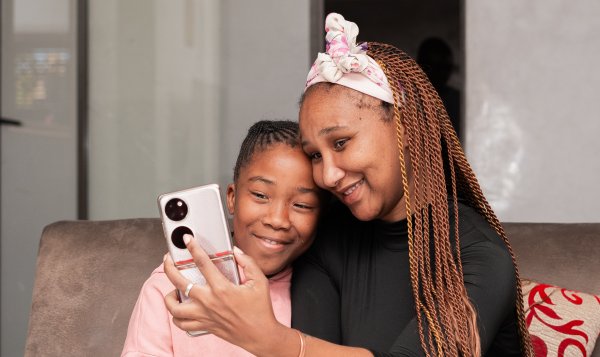 Portrait of black mother and daughter smiling on the couch taking a selfie.