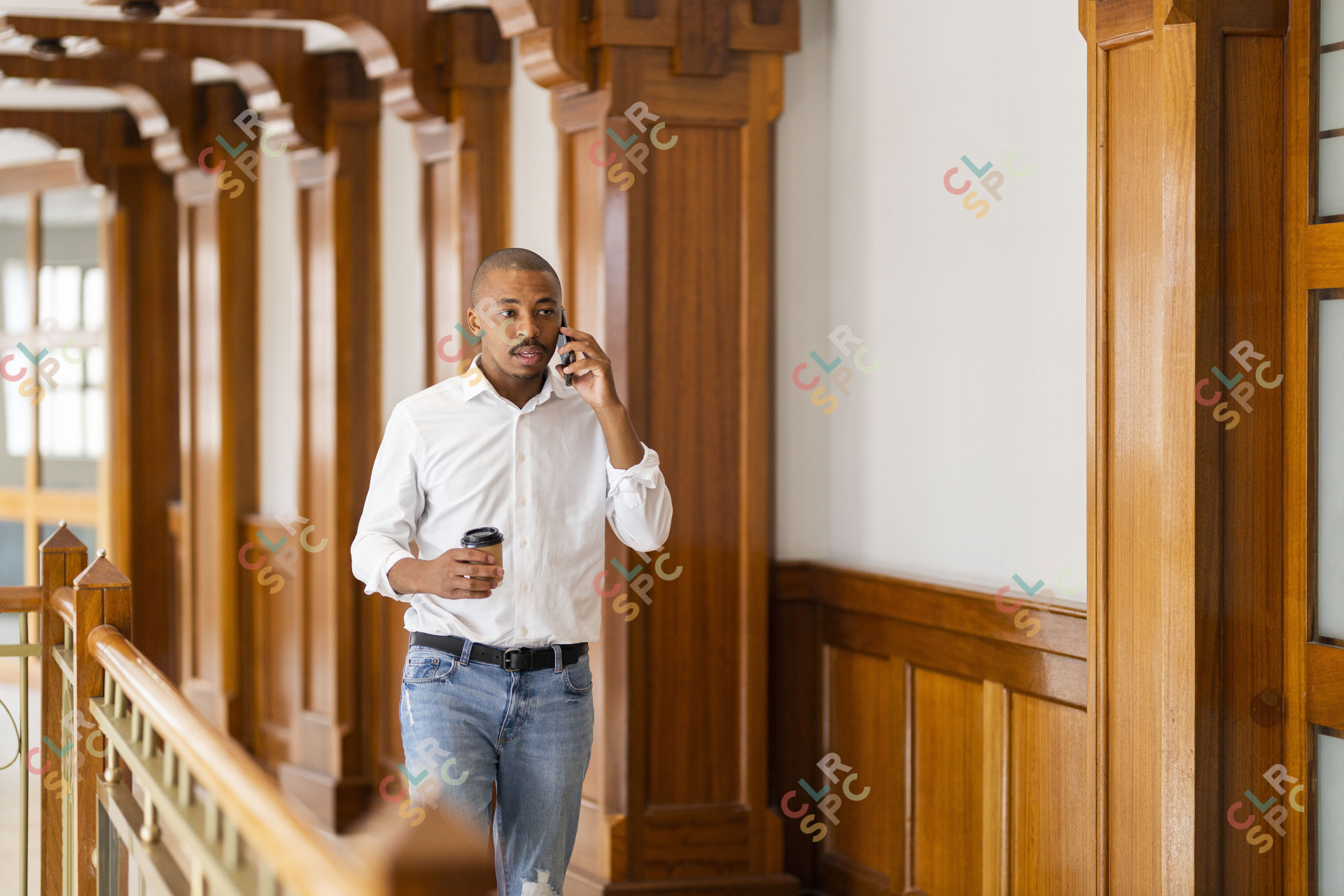 Black business man at work holding coffee and talking on the phone