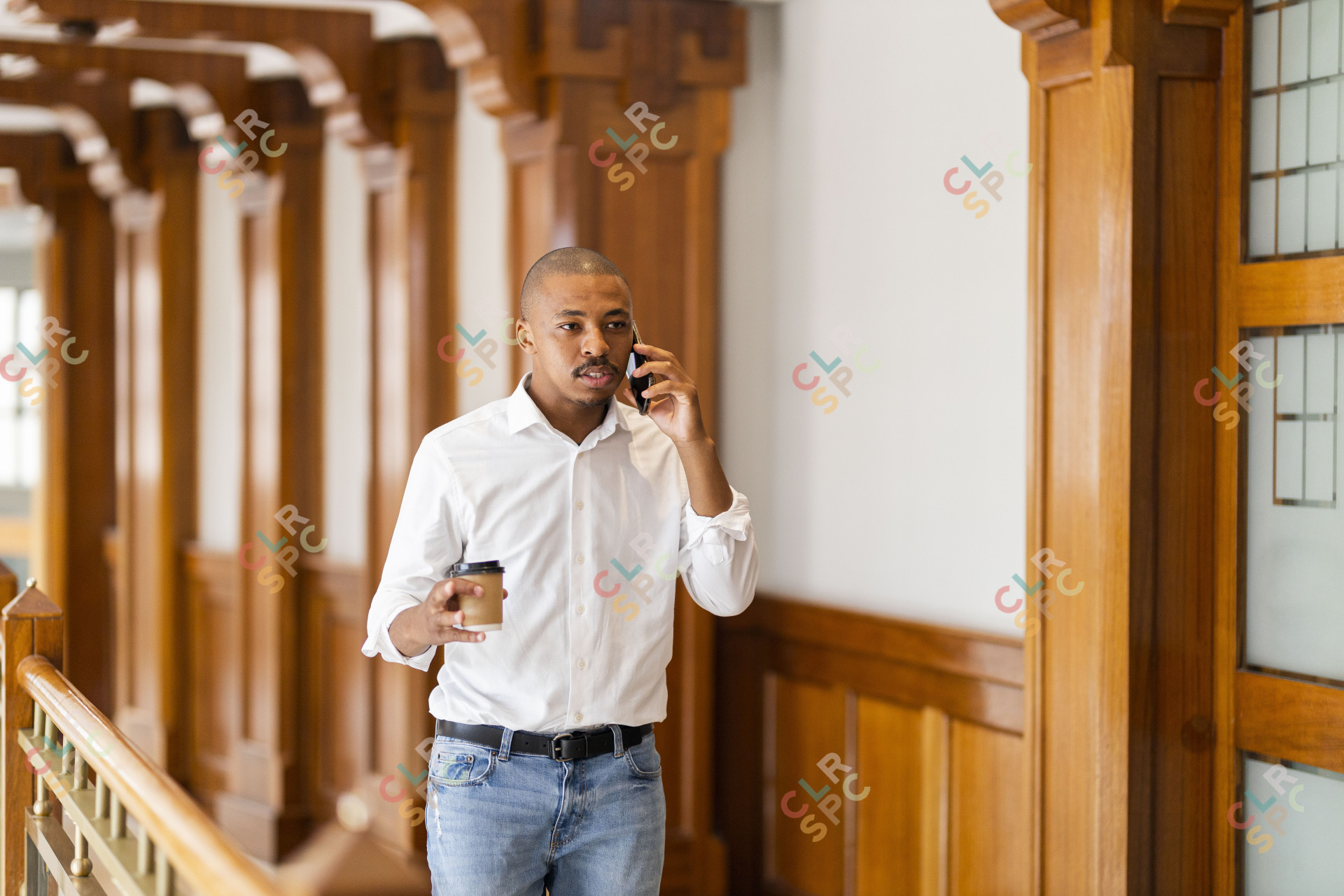 Black business man at work holding coffee and talking on the phone