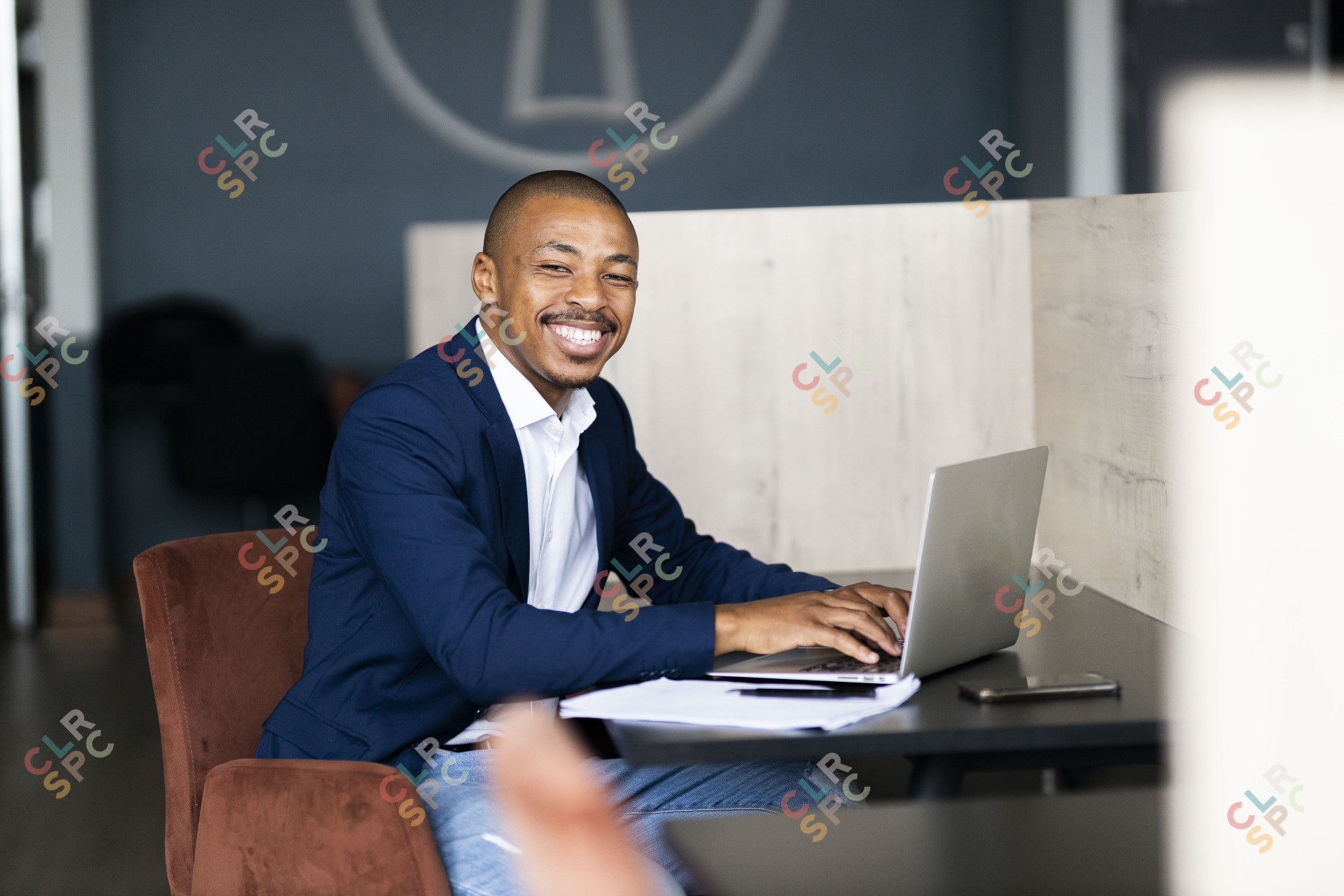 Black business man wearing a suit and looking at the camera while working on his laptop