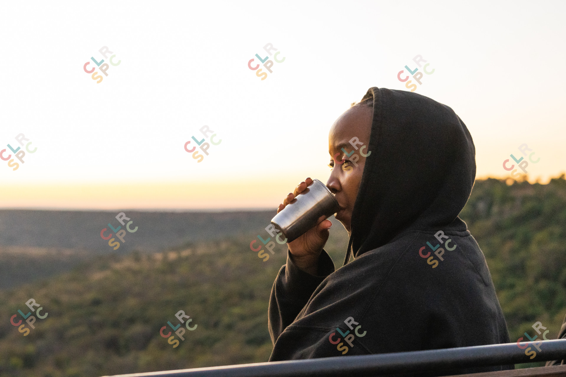 Black woman drinking coffee with a sunny background.