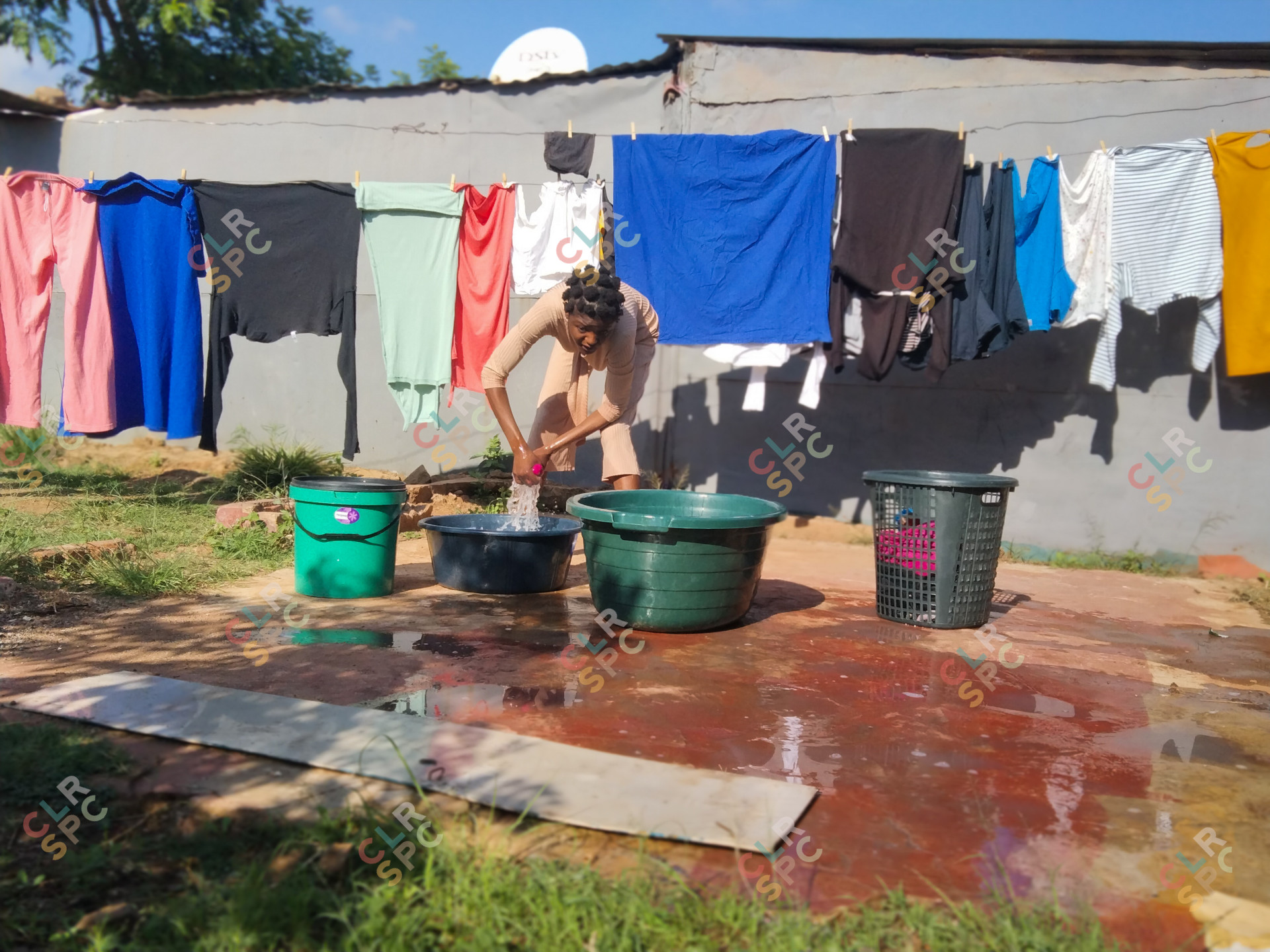 Black woman washing clothes outside her yard.