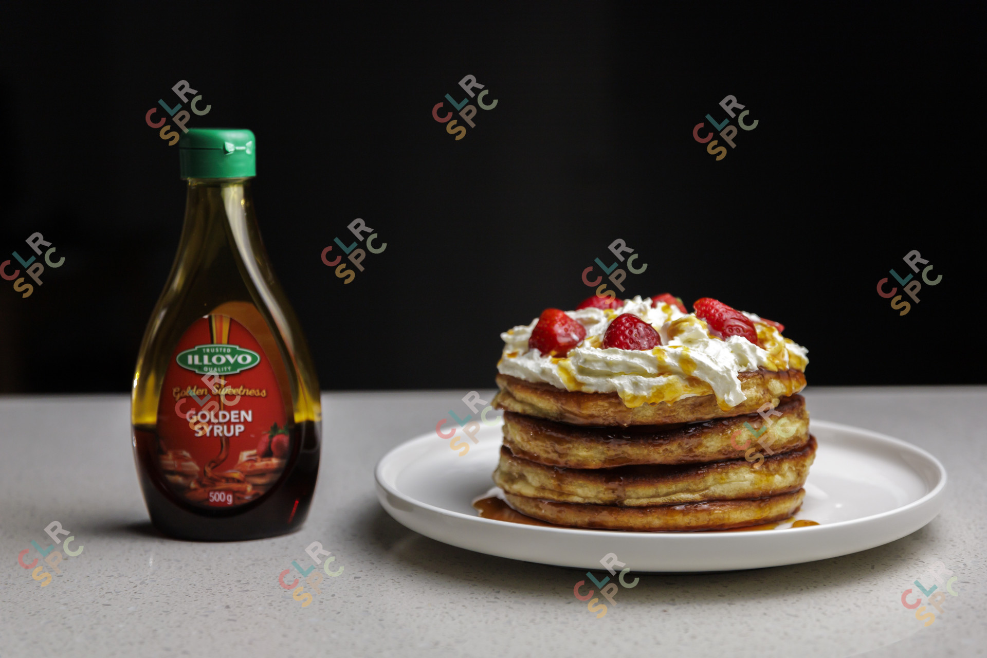 golden syrup bottle next to a plate of pancakes with strawberries and cream