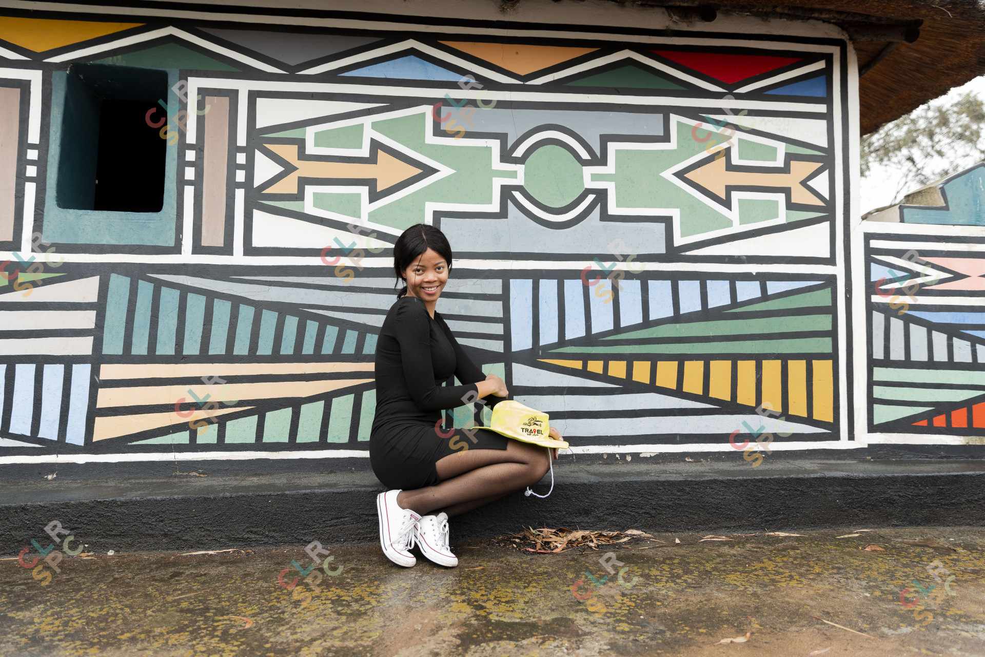 Black woman posing in front of Ndebele painting