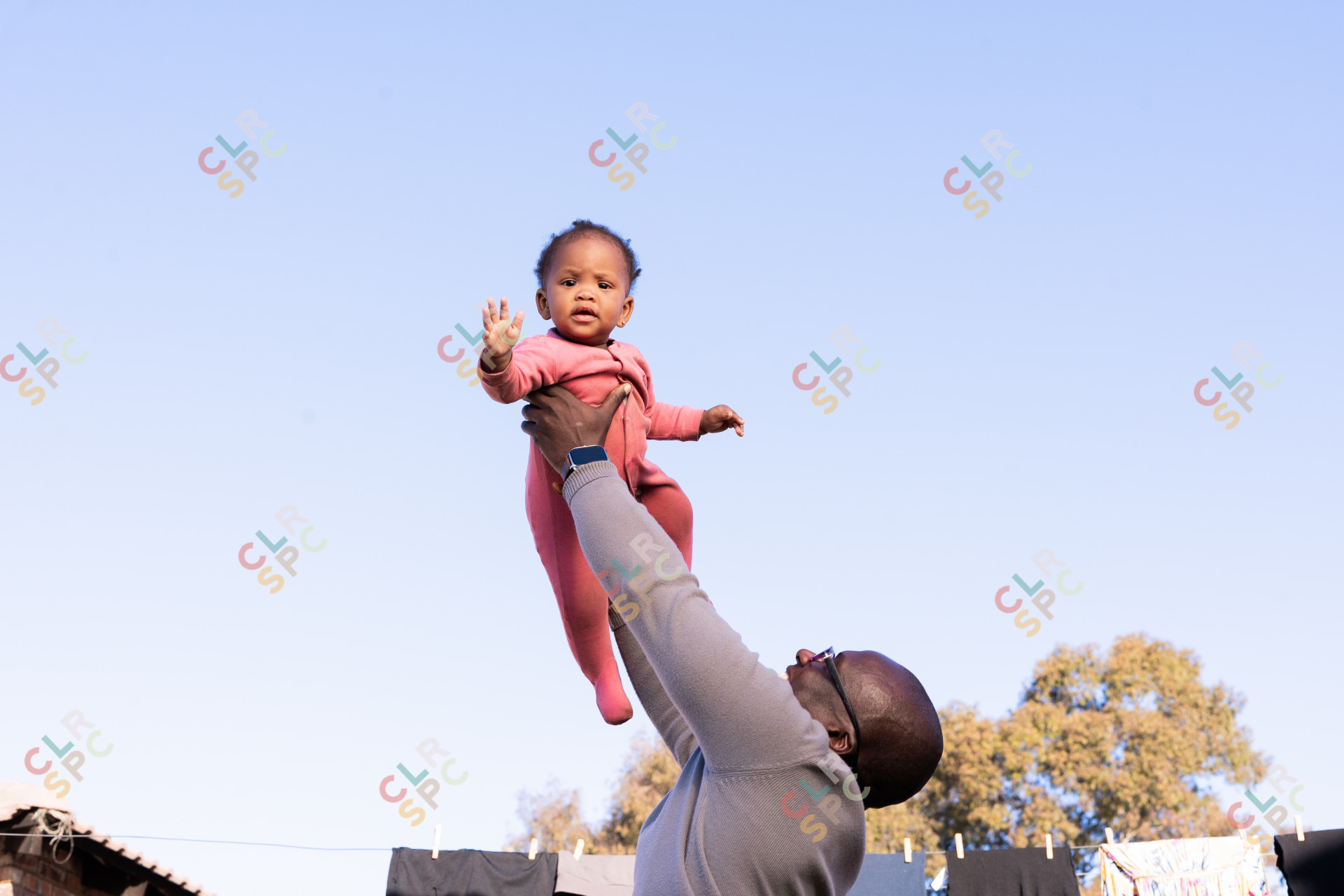 black daughter playing with father outdoors wearing pink with a blue sky in the background,