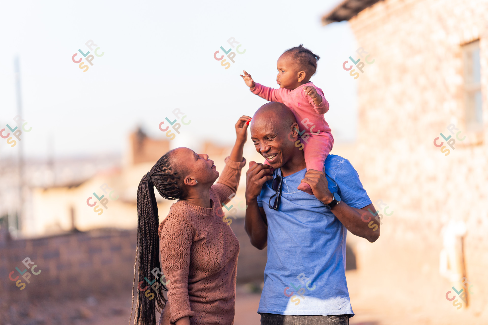 Black family with father and mother playing with daughter wearing pink, sunny day.