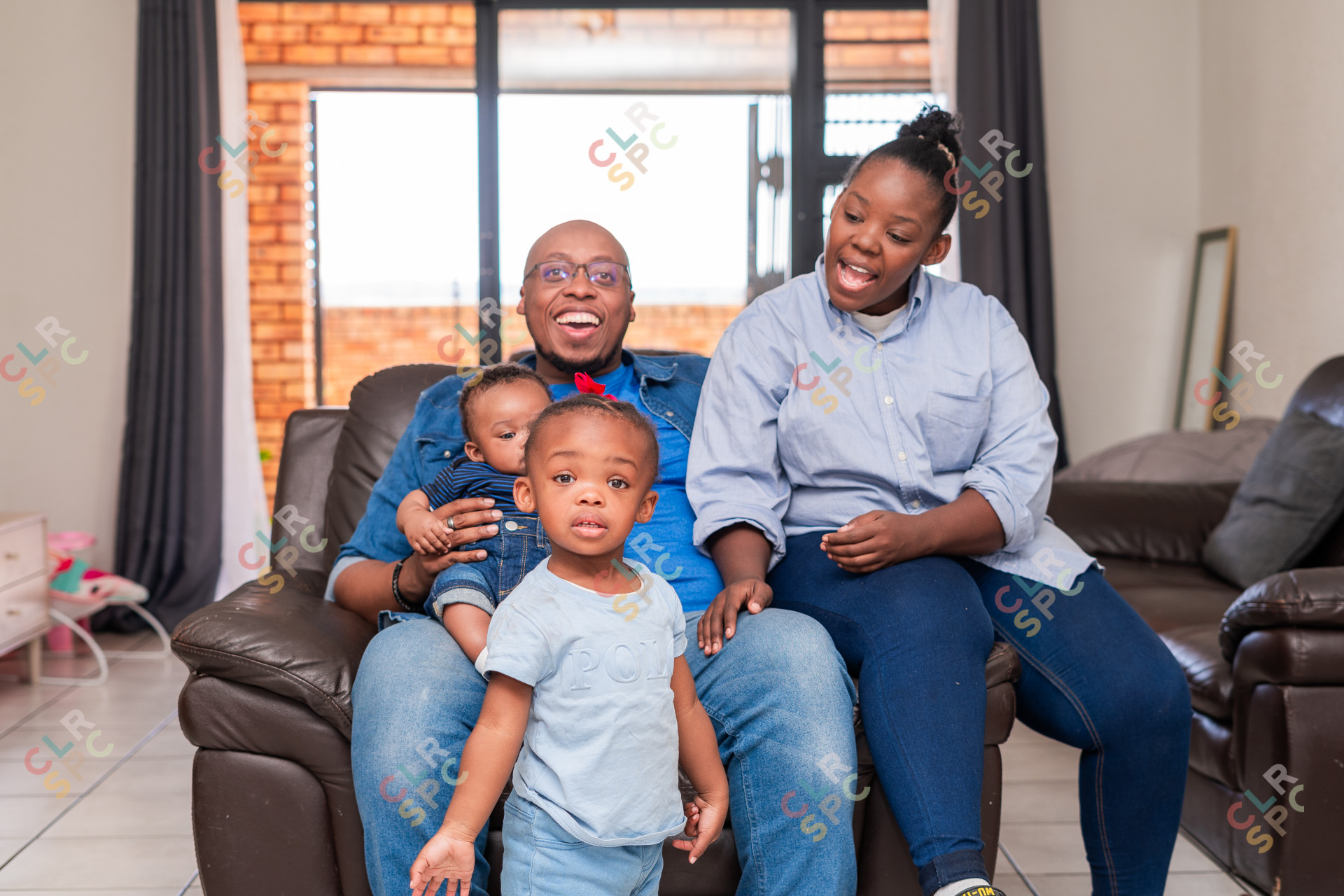 Toddler looking at camera in front of family at home on the couch.