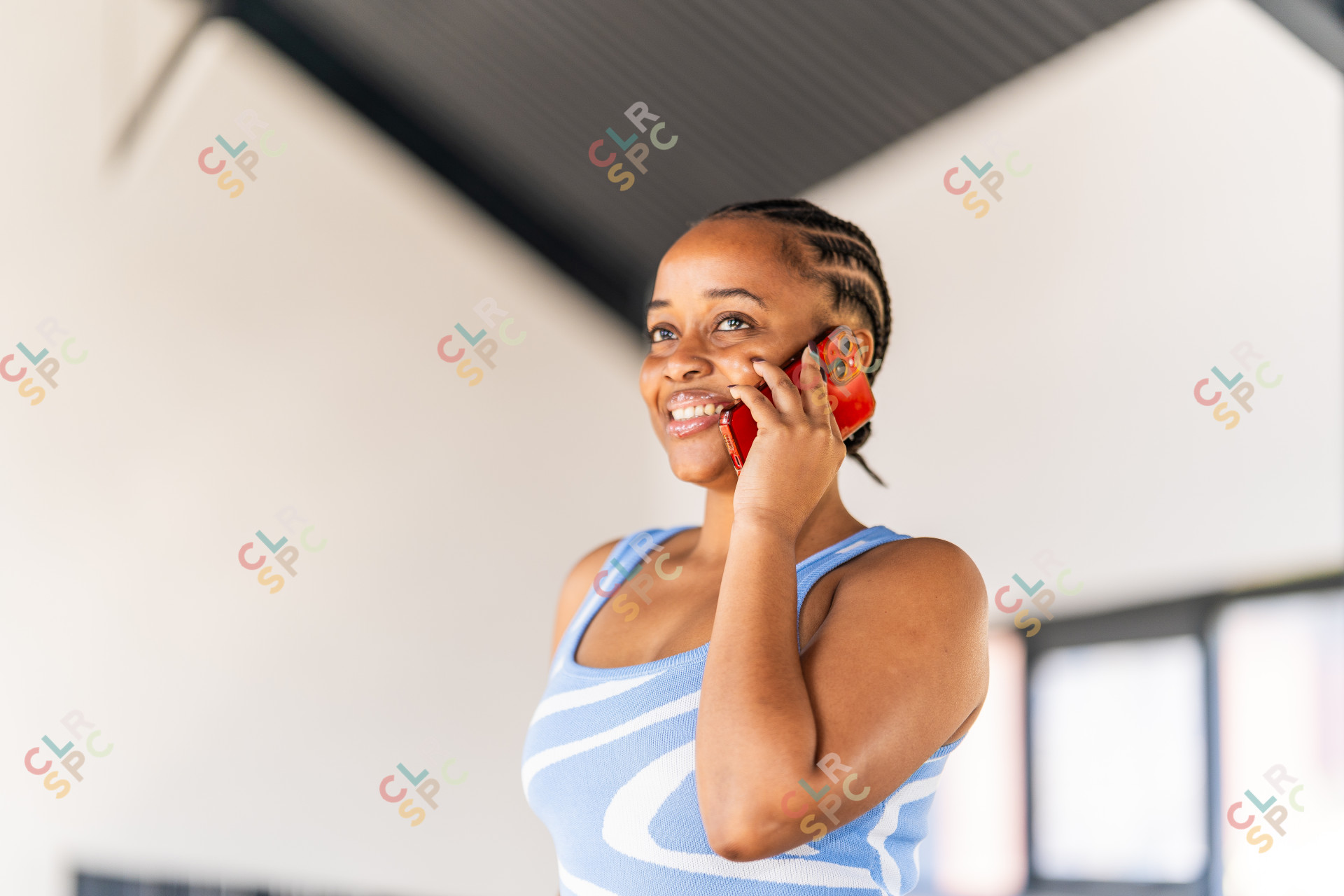 Black businesswoman talking on mobile phone smiling at the office with a blue top and braids.