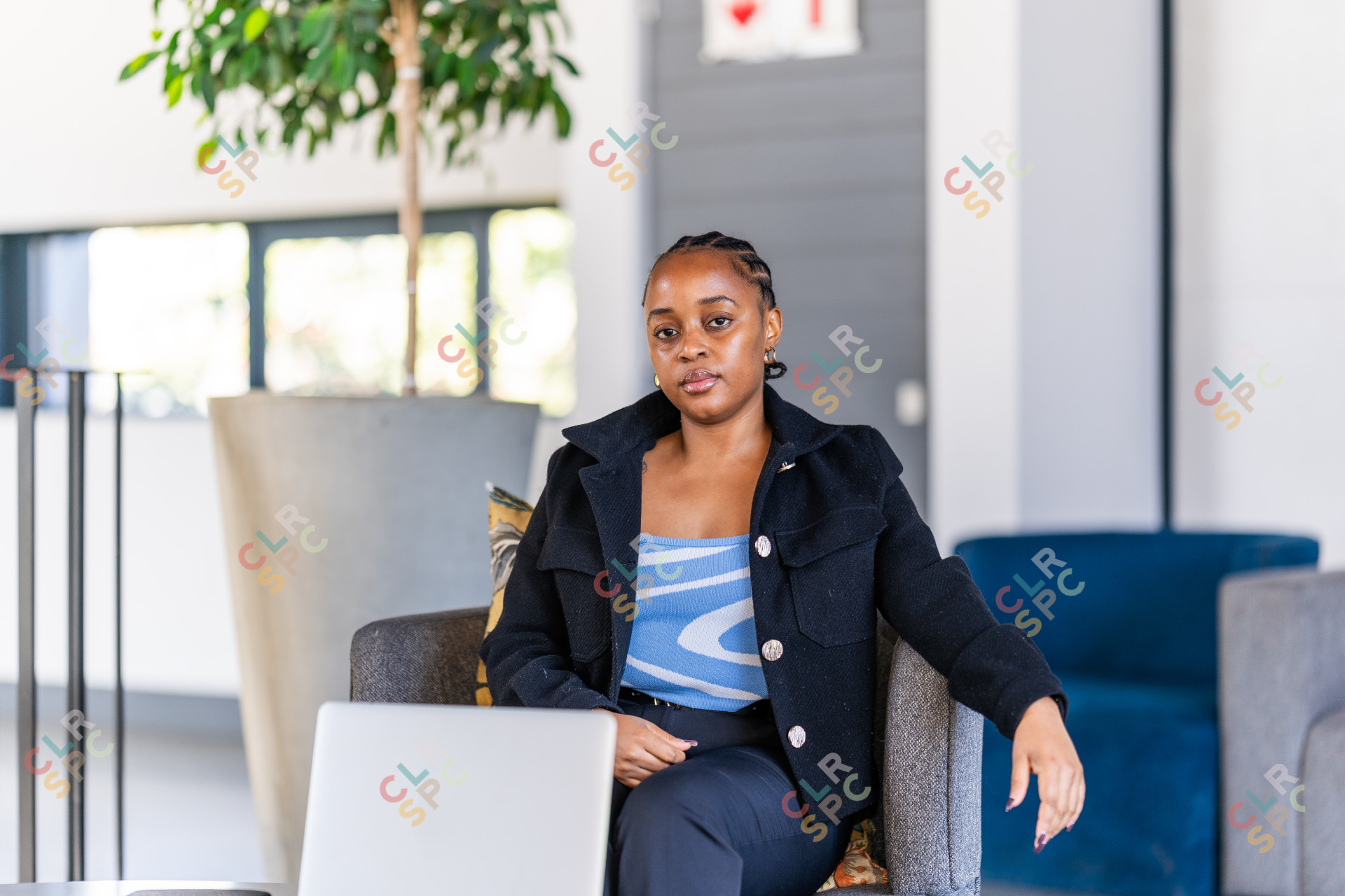 Young black woman sitting on the couch at work looking at the camera and a laptop in front of her.