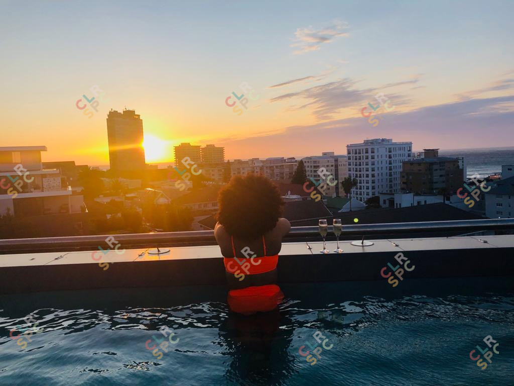 Black woman on a rooftop pool with a sunset