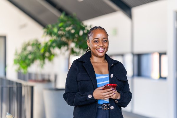 Professional black woman using a smart phone in an office. Happy business woman smiling at the camera with braids.