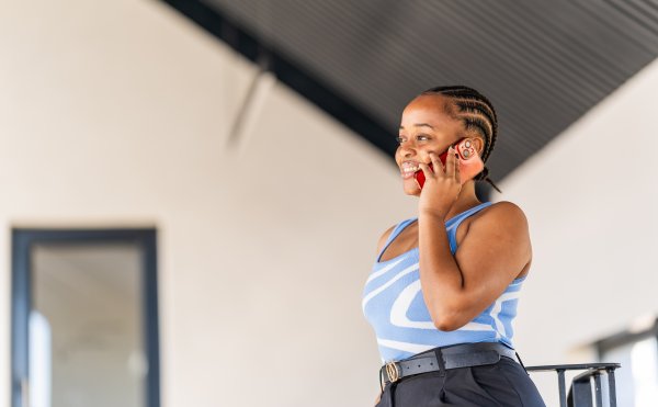 Young black woman on the phone smiling at the office with braids and a blue top.